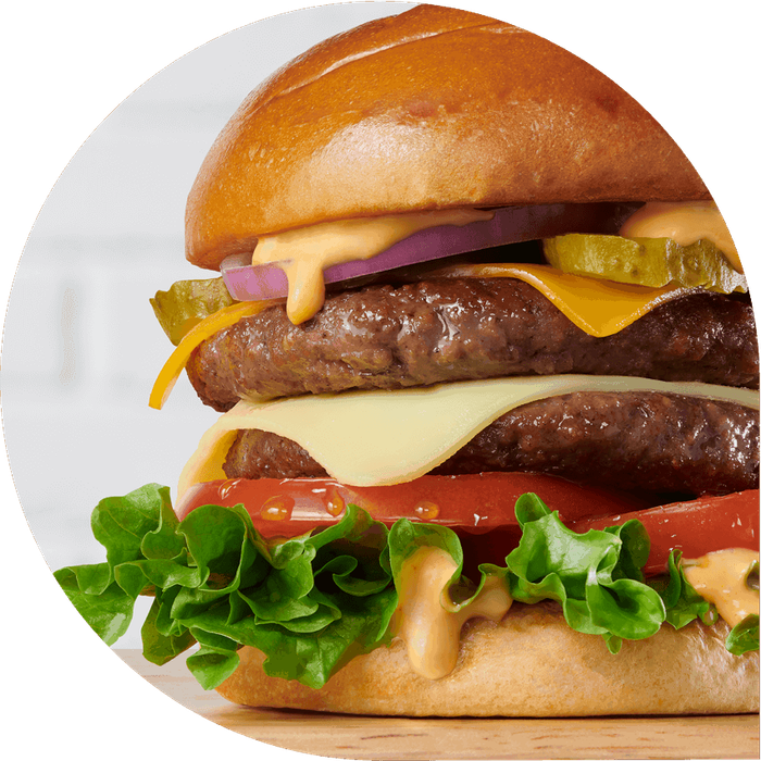 Juicy plant-based burger with tomato, lettuce, cheese, and pickles on a whole wheat bun.